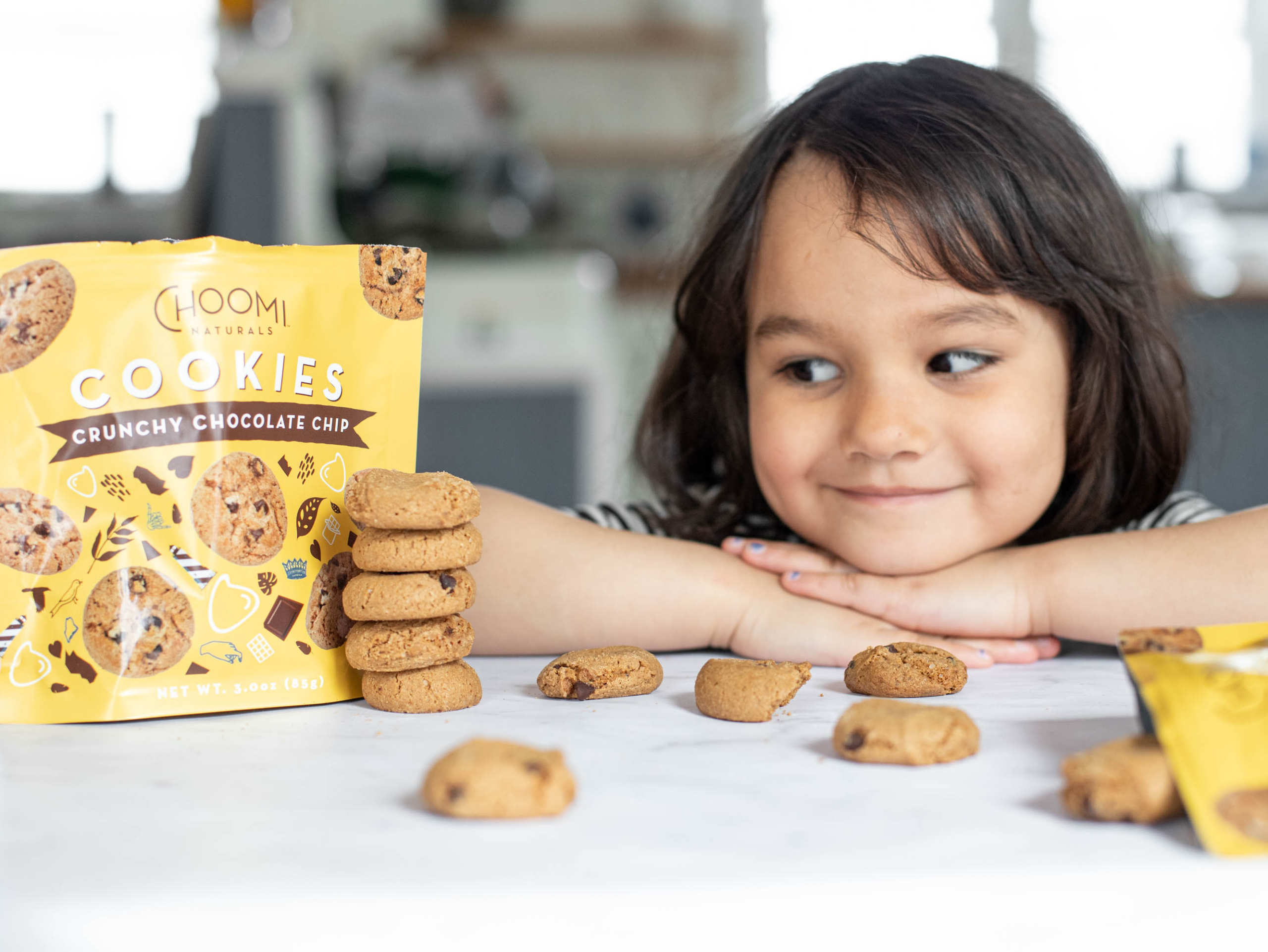 Child looking at Choomi Crunchy Chocolate Chip bag with a smile