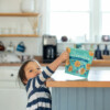 Child reaching for a package of Choomi Chocolate Chip Macaroons off a tabletop